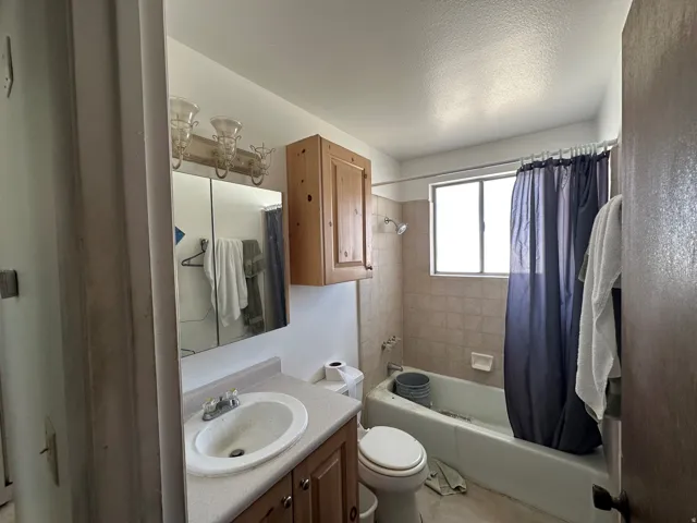 Bathroom featuring a built-in vanity with integrated sink, wall-mounted light fixture, recessed medicine cabinet, and a bathtub with tiled surround