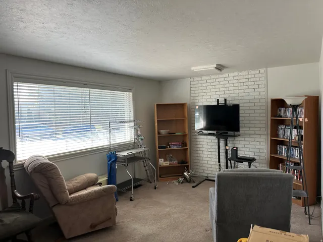 Expansive window with horizontal blinds, textured ceiling, wall featuring a white brick-style finish, and carpeted flooring