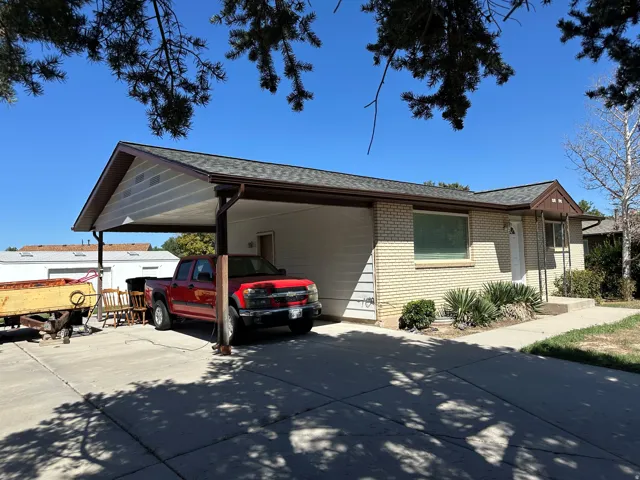 Brick and siding exterior with a covered carport, concrete driveway, and mature landscaping
