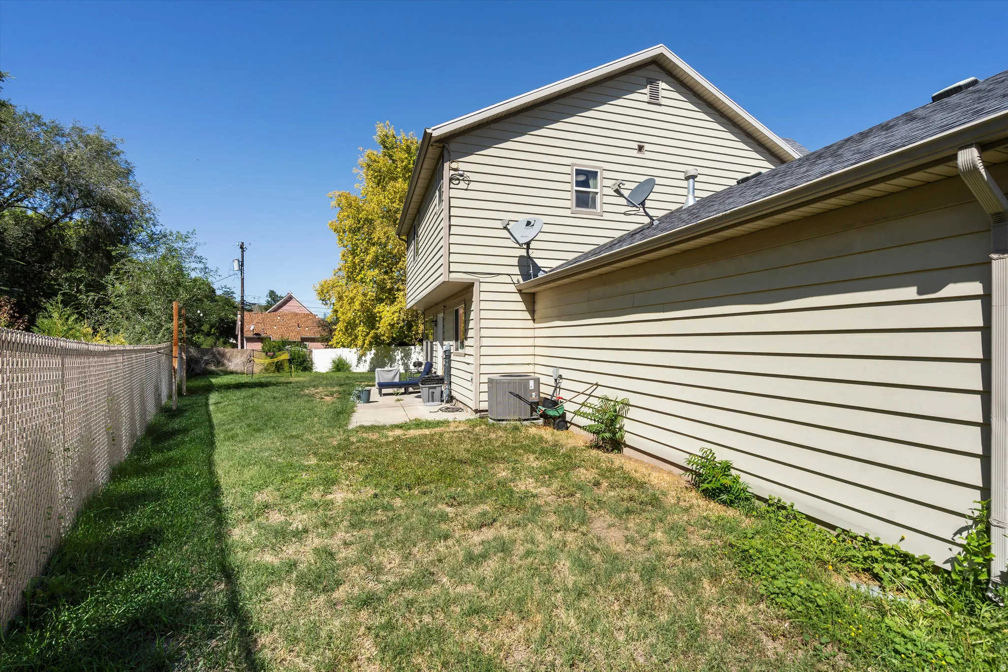 Expansive rear yard featuring a chain-link fence, a concrete patio, and a light-colored siding exterior