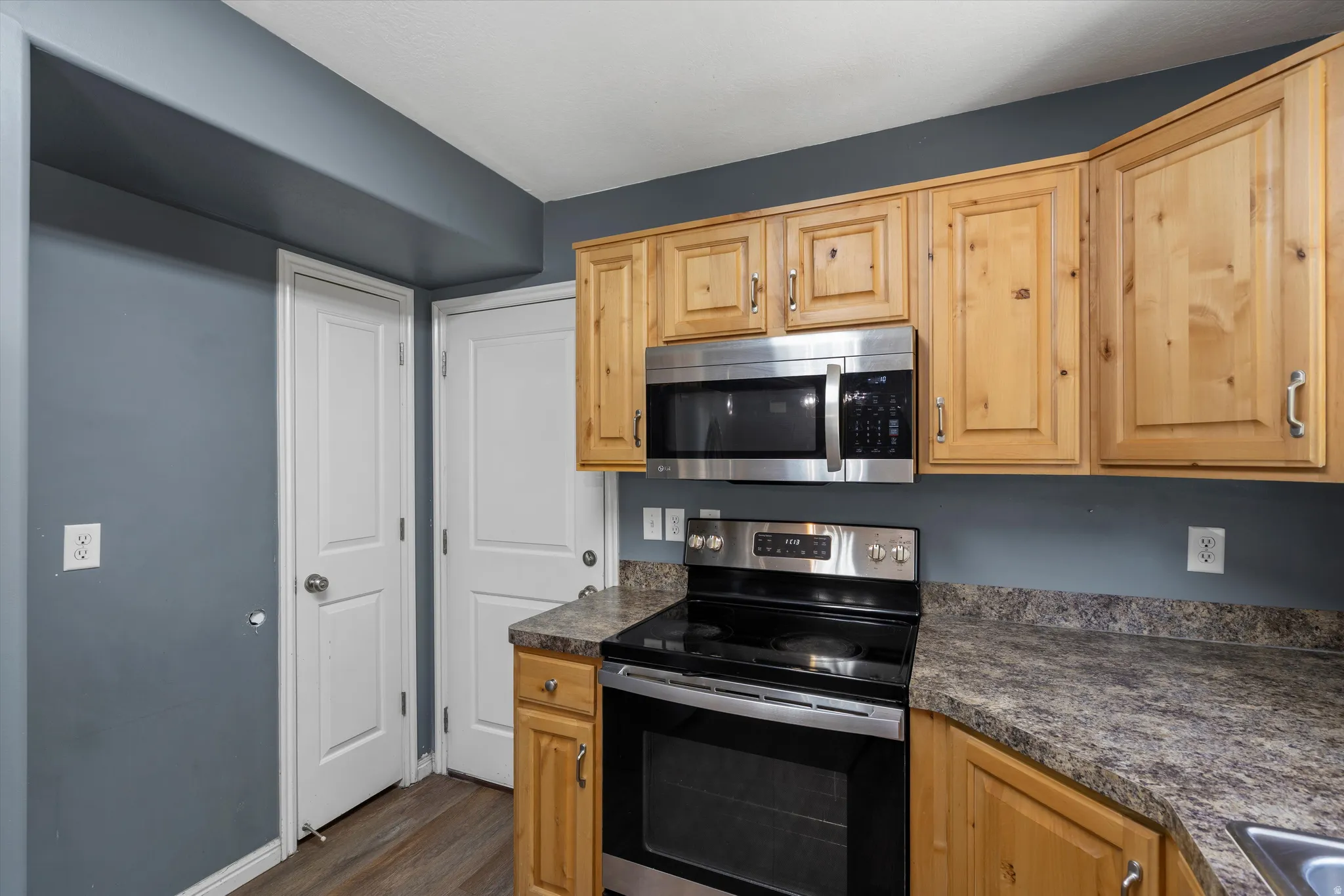 Kitchen featuring wood cabinetry, stainless steel appliances, speckled countertops, and wood-finish flooring