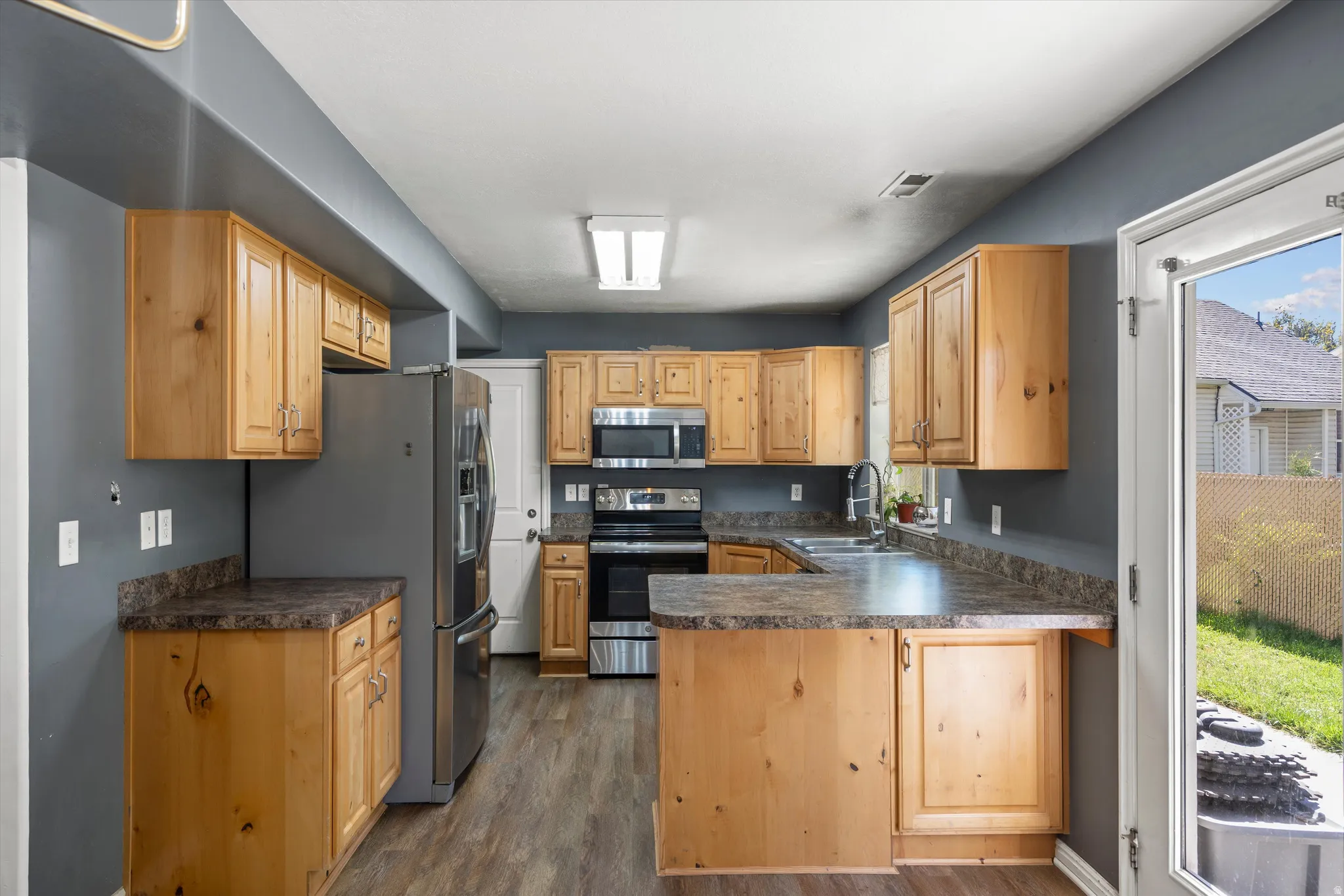 Kitchen featuring wood-finish cabinetry, dark countertops, stainless steel appliances, and wood-finish flooring