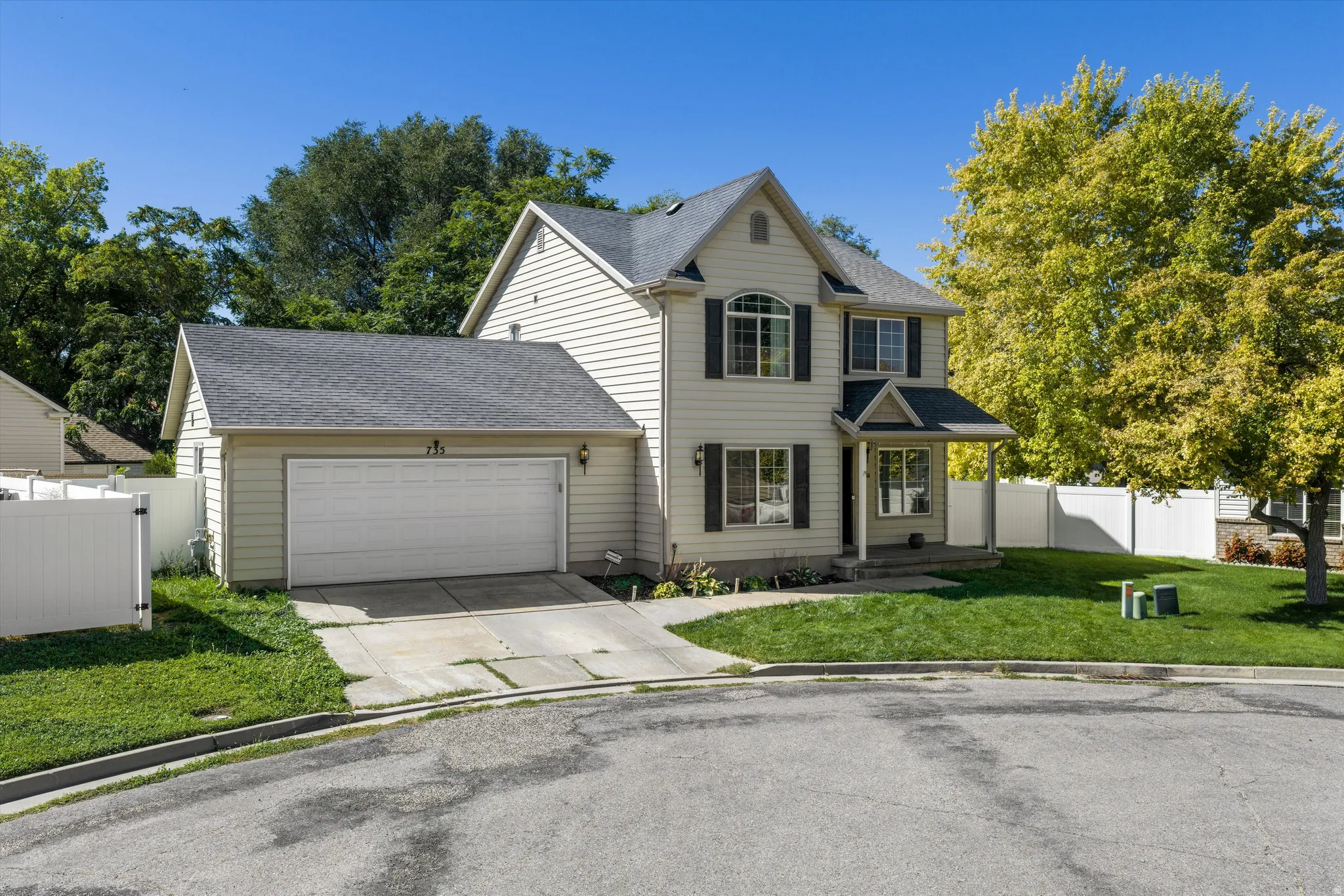 Two-story residence with a covered front porch, attached garage, and white vinyl fencing
