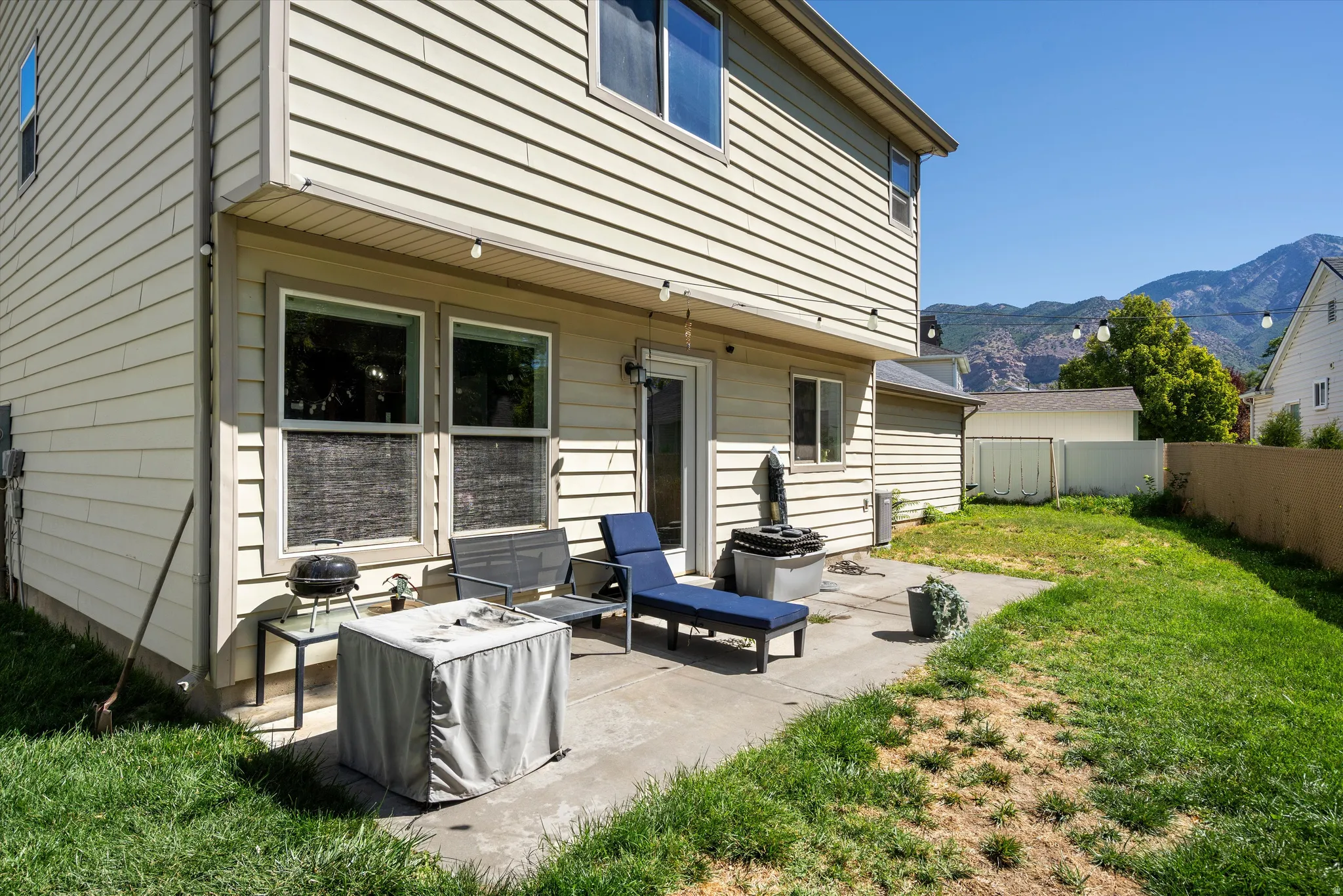 Rear exterior with a concrete patio, expansive lawn, and mountain backdrop