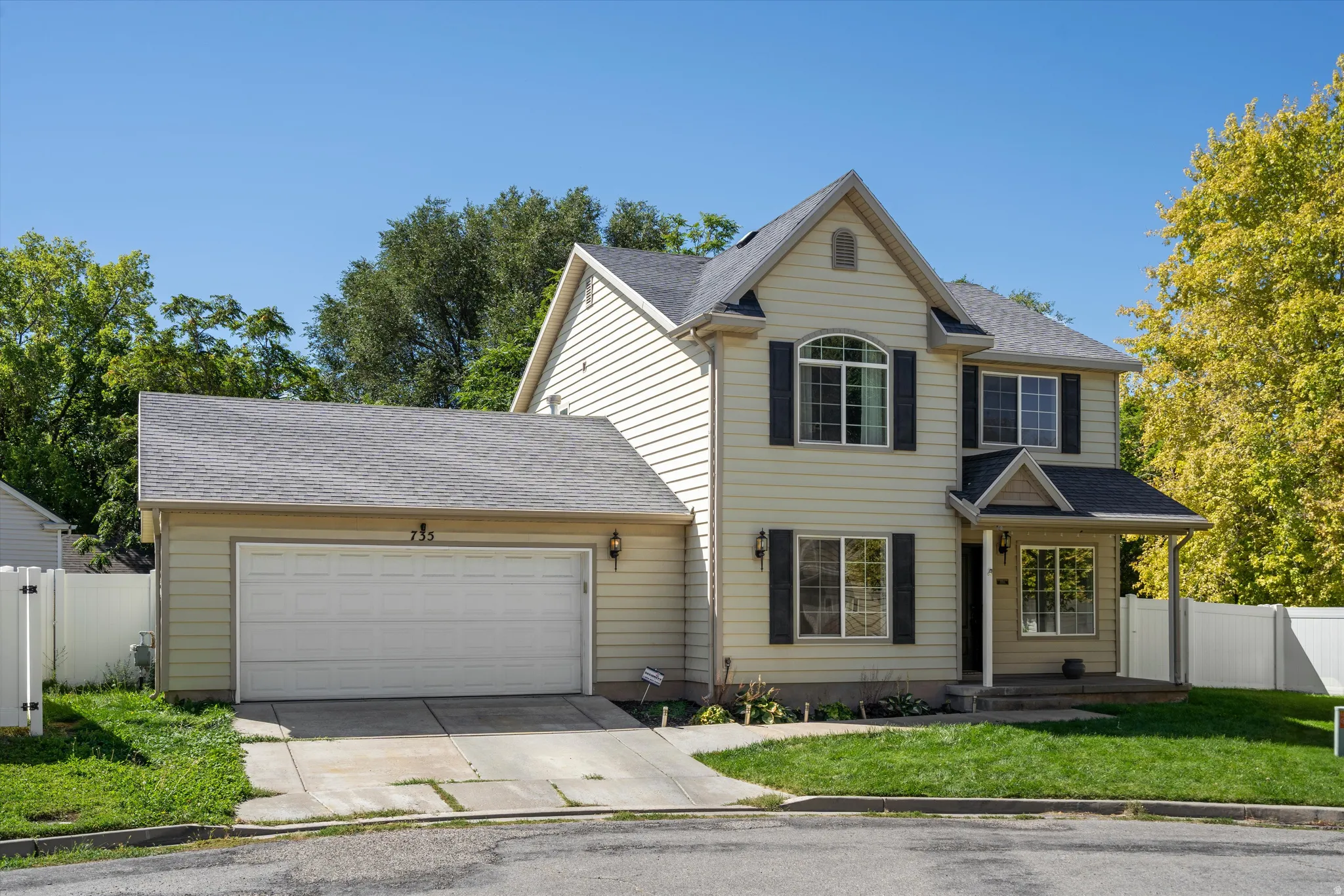 Two-story property featuring light-colored siding, a covered front entry, and a two-car garage with an asphalt driveway