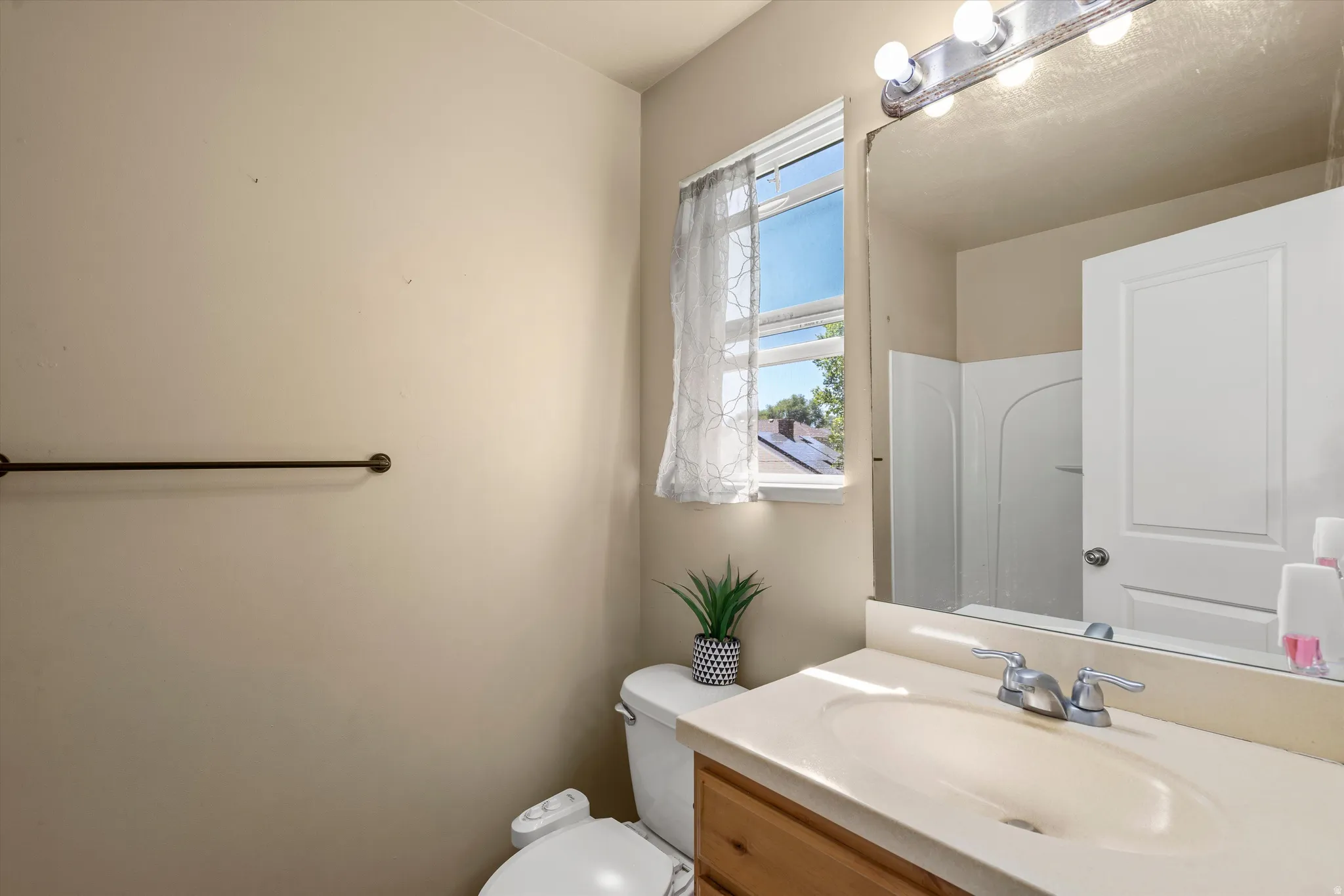 Bathroom featuring a single-sink vanity with light-colored countertop, wood-finish cabinetry, and an integrated mirror with overhead lighting