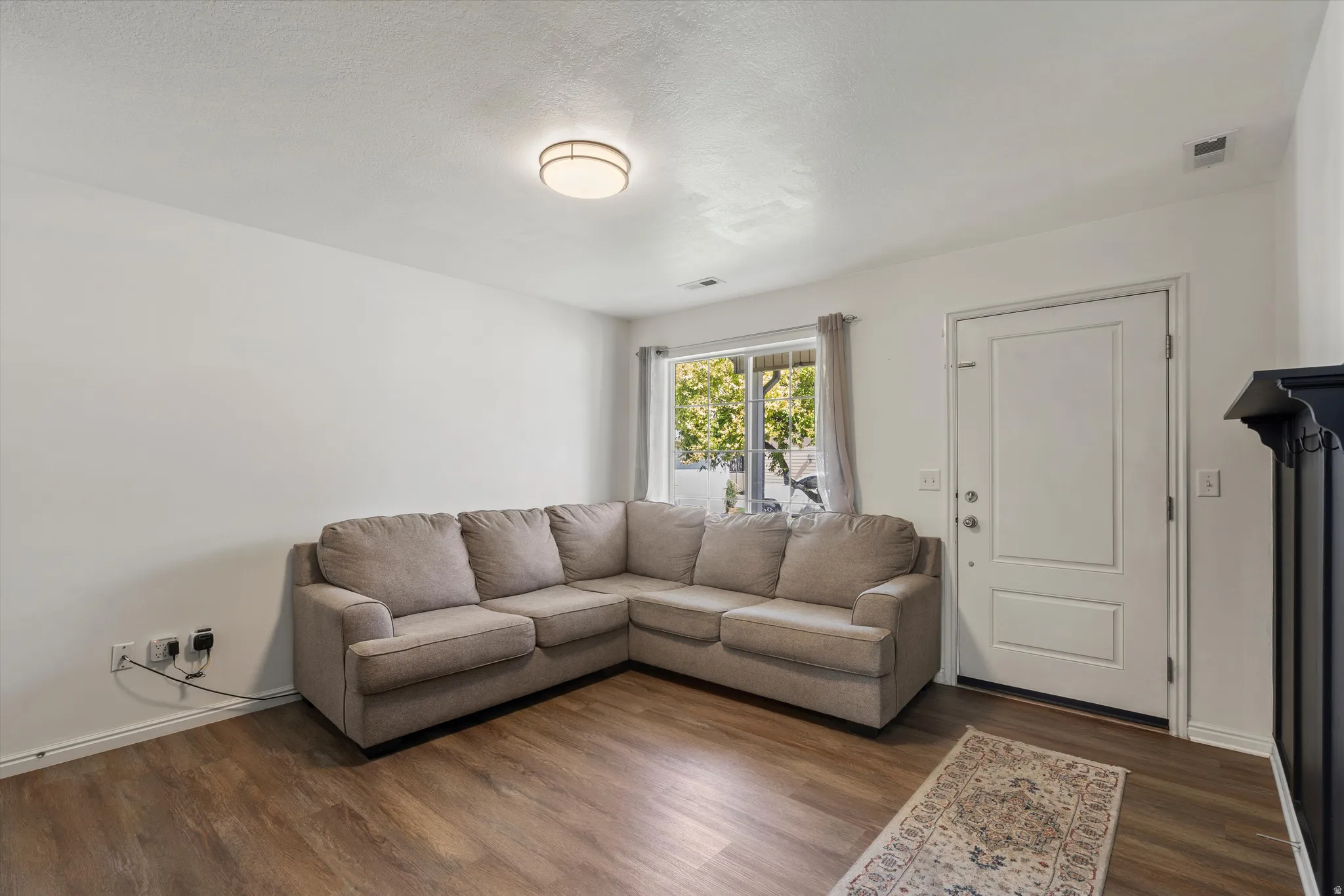 Wood-finish flooring, white walls, and a recessed window with neutral curtains