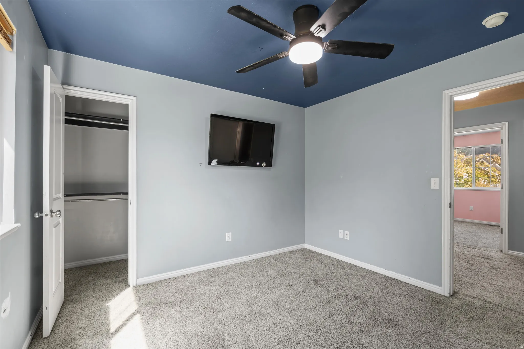 Recessed closet with shelving, ceiling-mounted fan, wall-mounted television, and light gray carpet flooring