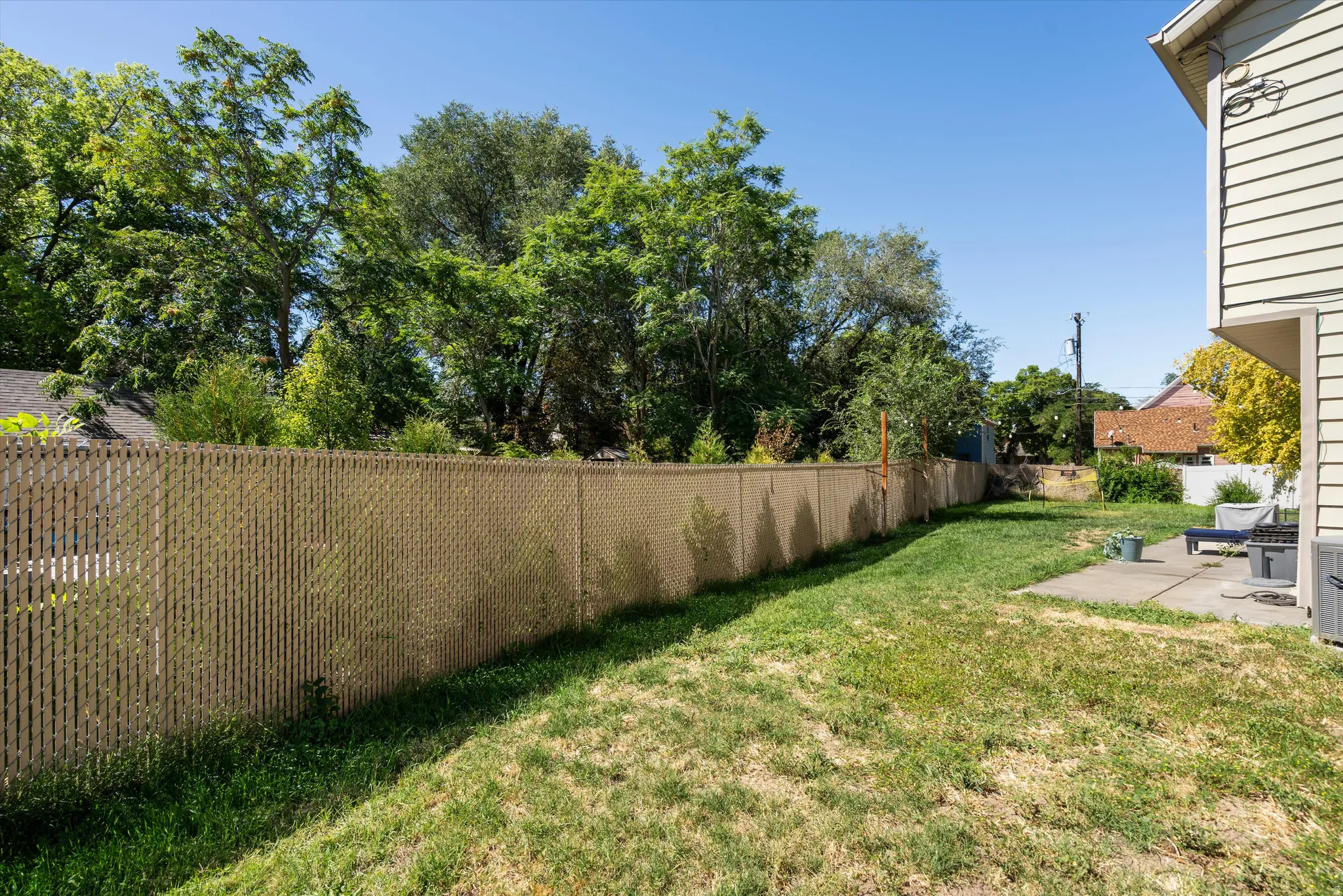 Expansive side yard featuring a chain-link fence with privacy slats, mature trees, and a concrete patio