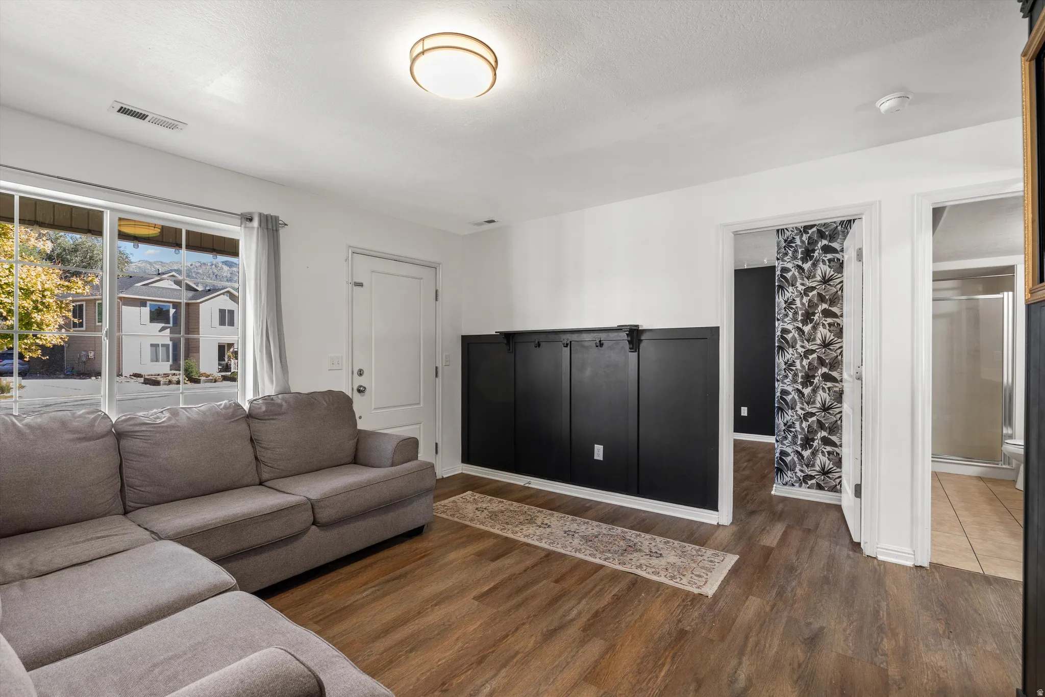 Wood-finish flooring, built-in black wainscoting with integrated hooks, white interior doors, and a transparent glass shower enclosure