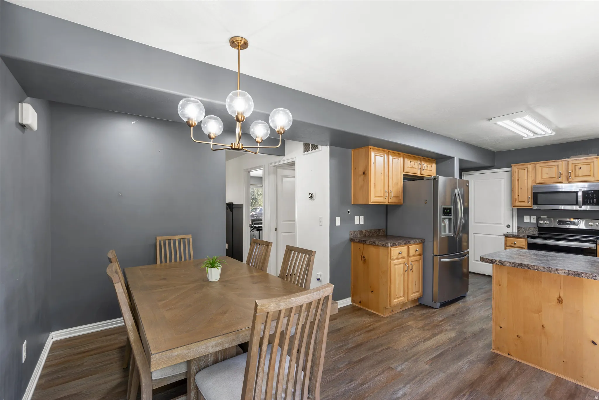 Wood-finish flooring throughout, brushed gold chandelier, stainless steel refrigerator, built-in stainless steel microwave, and wood cabinetry