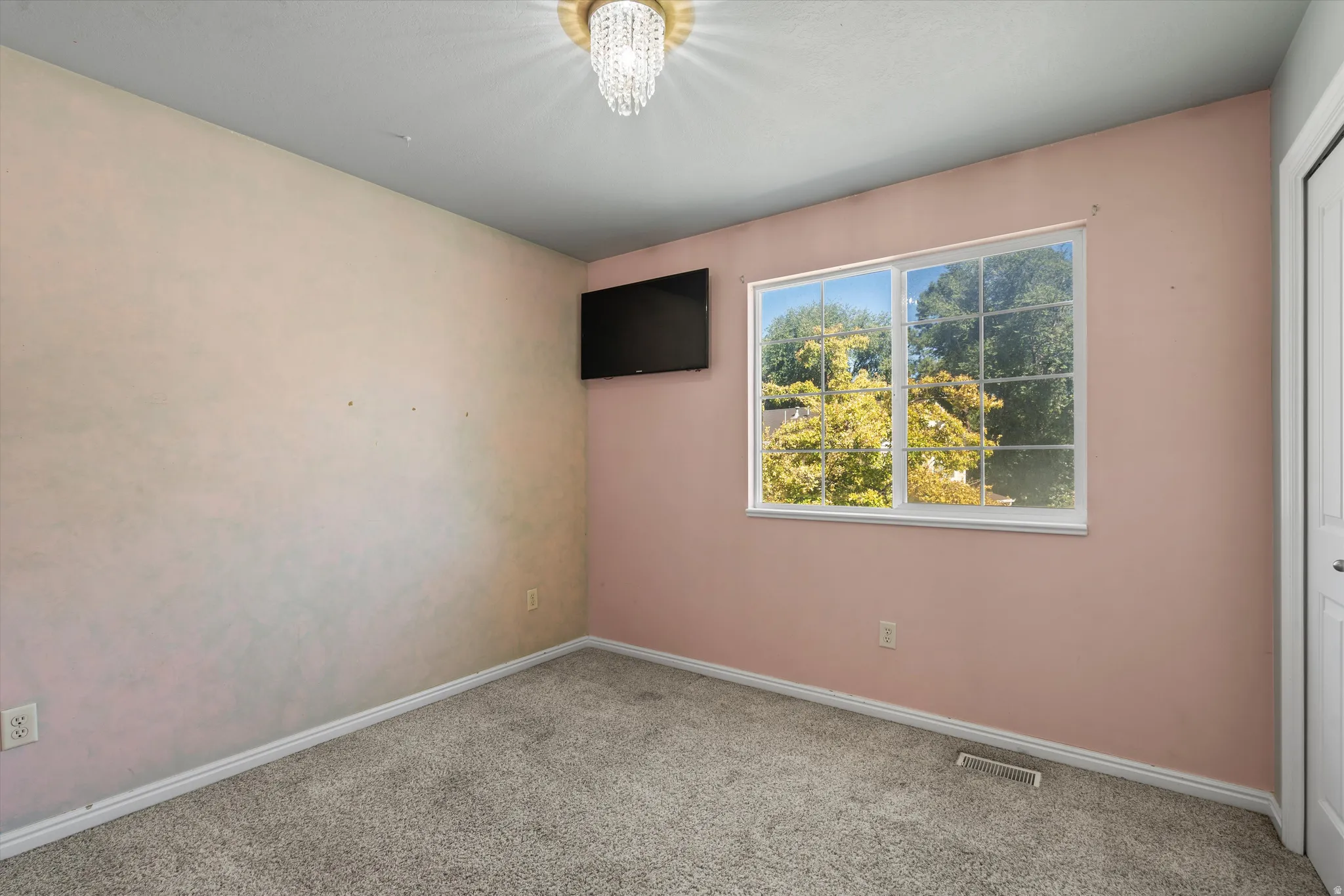 Window with white frame, wall-mounted television, and flush-mount chandelier