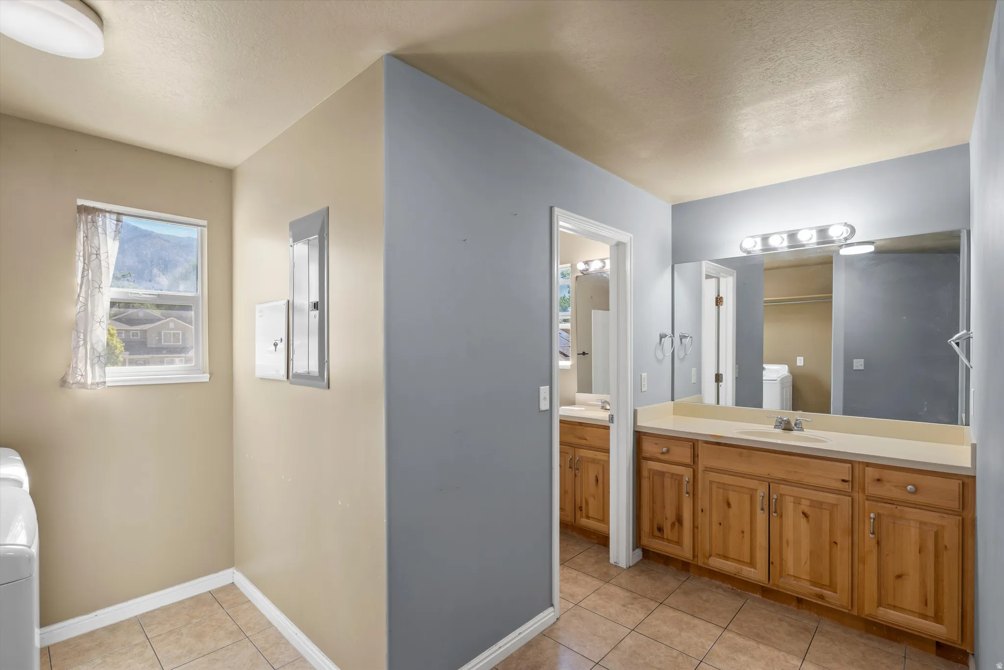 Dual vanity with wood-finish cabinetry and integrated sinks, complemented by a large wall-mounted mirror and overhead lighting