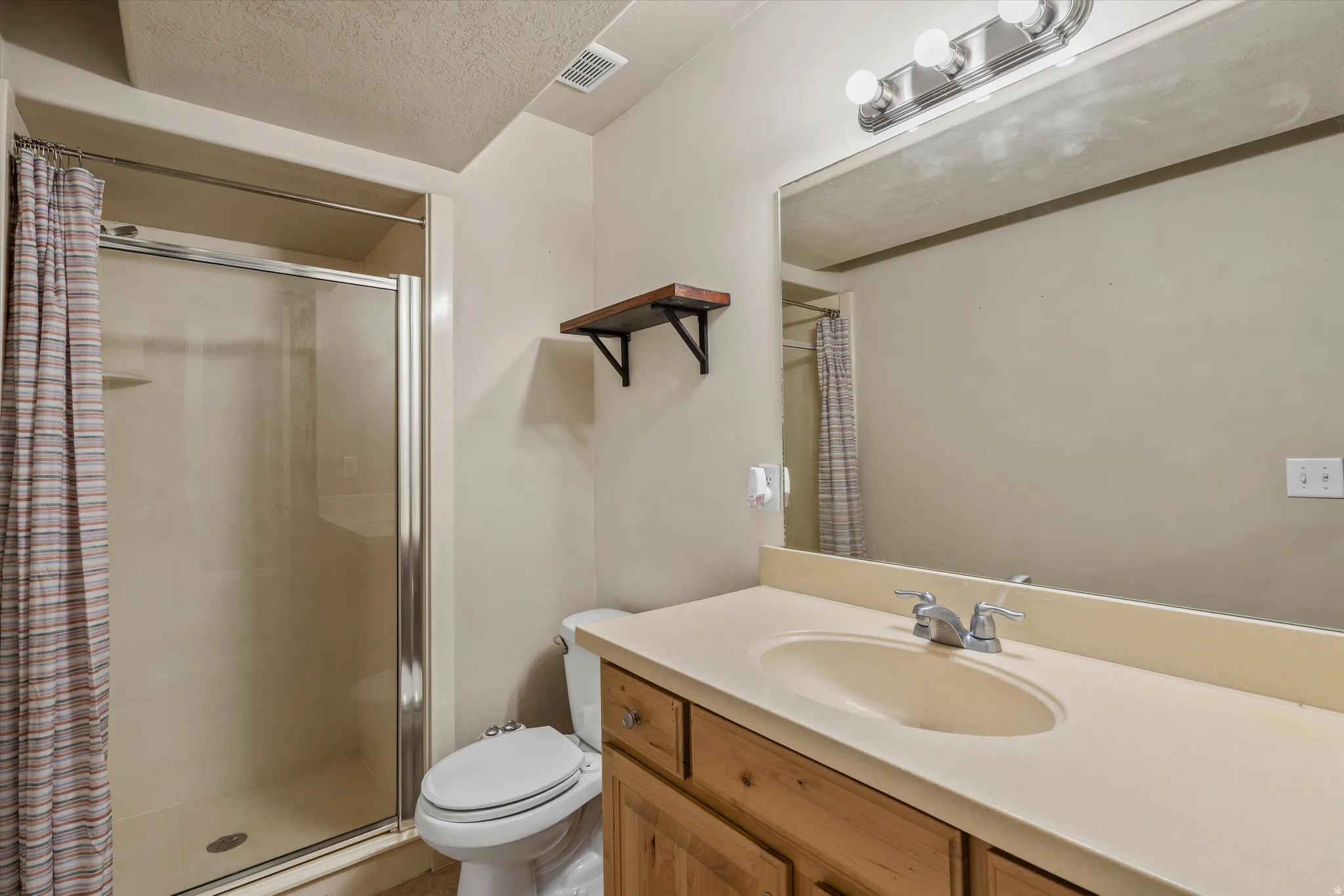 Bathroom featuring a shower with glass enclosure, wood-finish vanity, integrated sink, wall-mounted mirror, and overhead vanity lighting