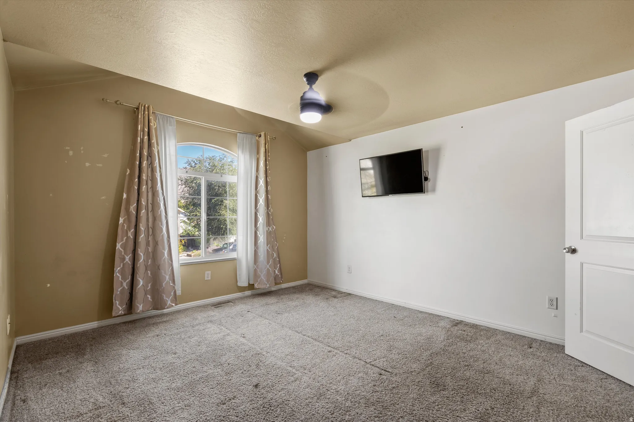 Arch-top window with surrounding drapery, sloped ceiling, and ceiling-mounted light fixture