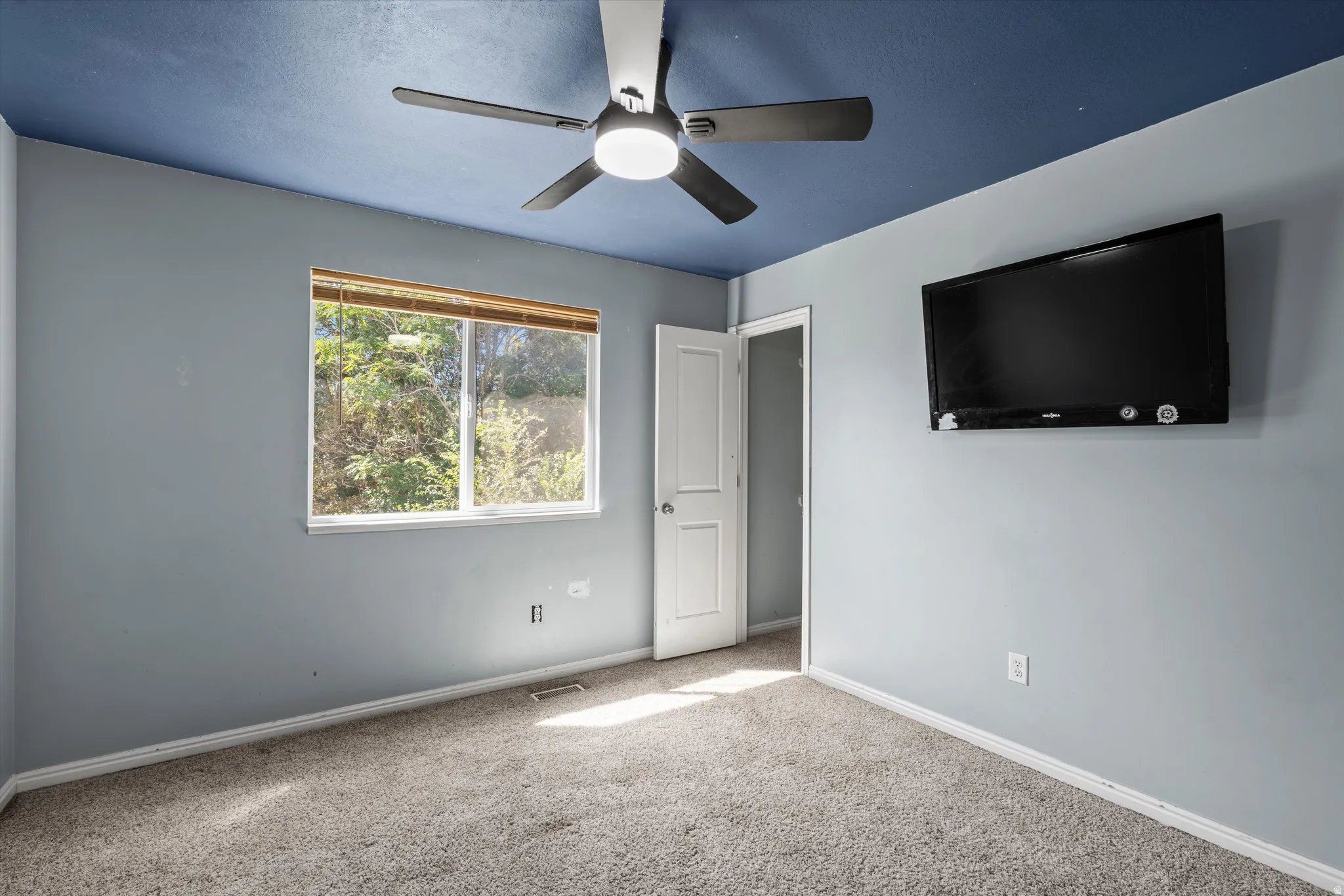 Wall-mounted television with a ceiling fan, a window, and a door