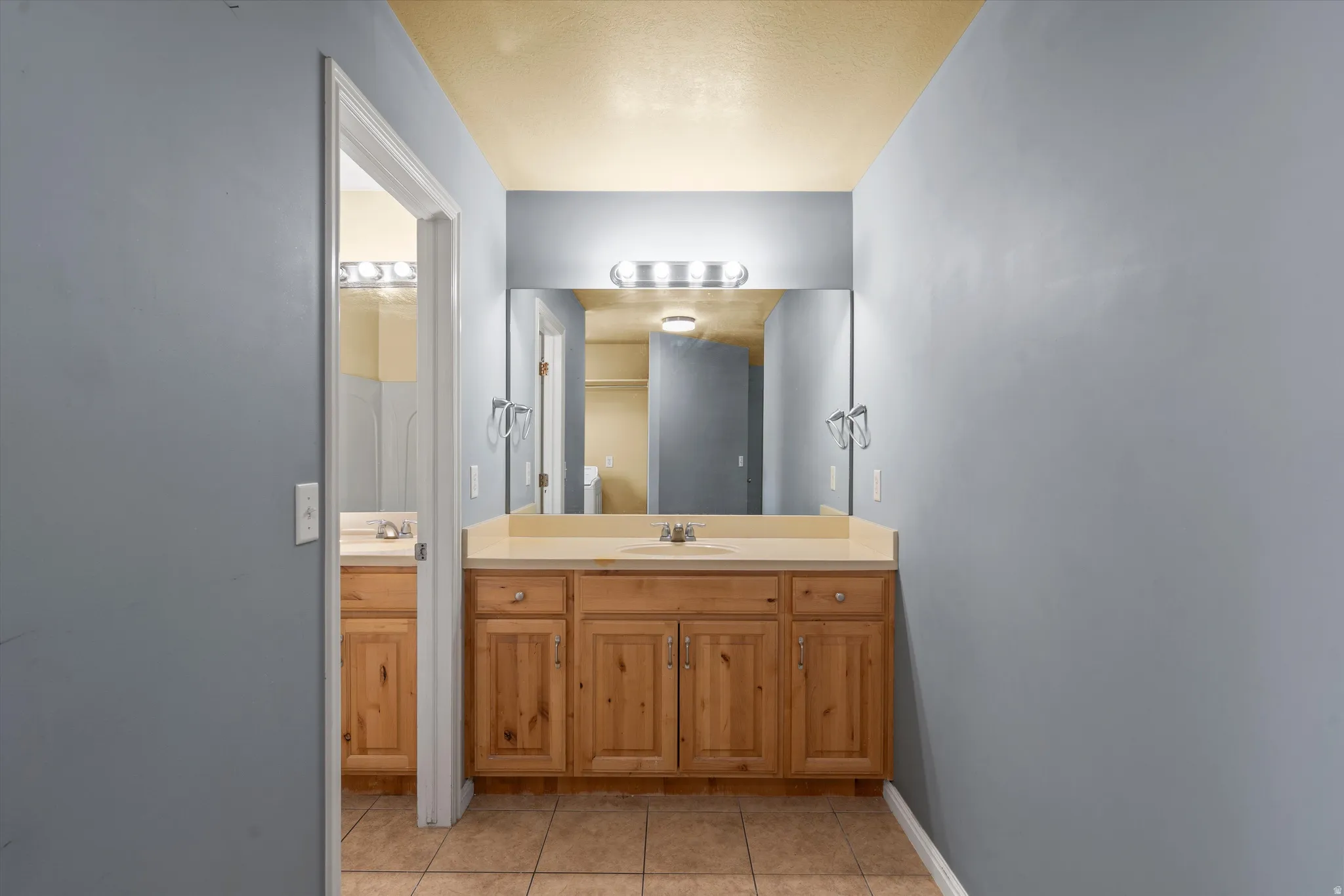 Dual wood-finish vanities with light countertops, individual mirrors, and bar lighting fixtures
