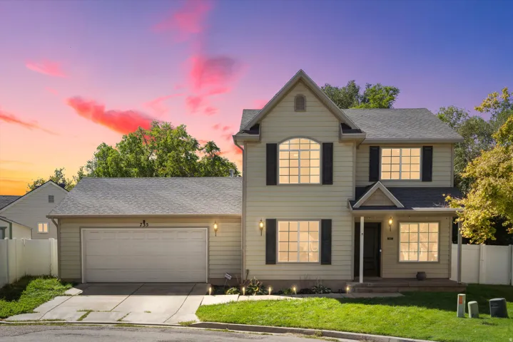 Two-story residence featuring light-colored siding, a two-car garage, and dark window shutters