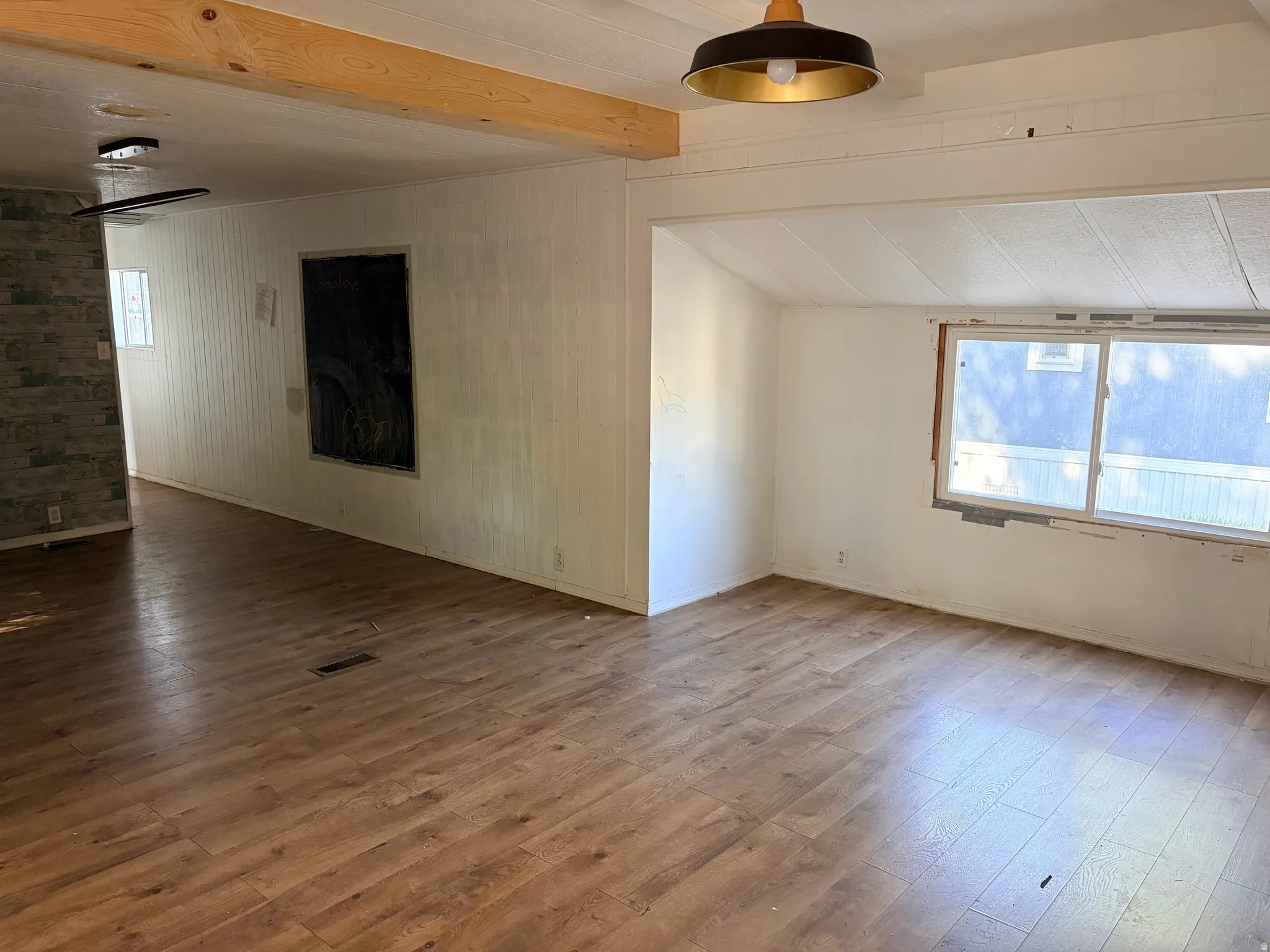 Wood-finish flooring throughout, exposed ceiling beam, recessed lighting, and a large window