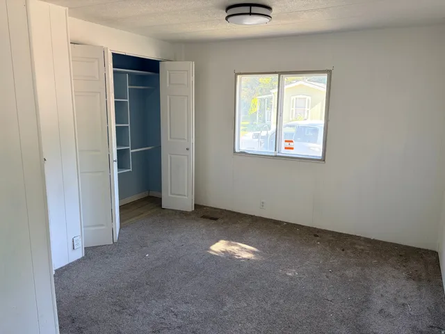 Built-in closet with bifold doors and shelving, overhead flush-mount lighting, and an aluminum-framed window