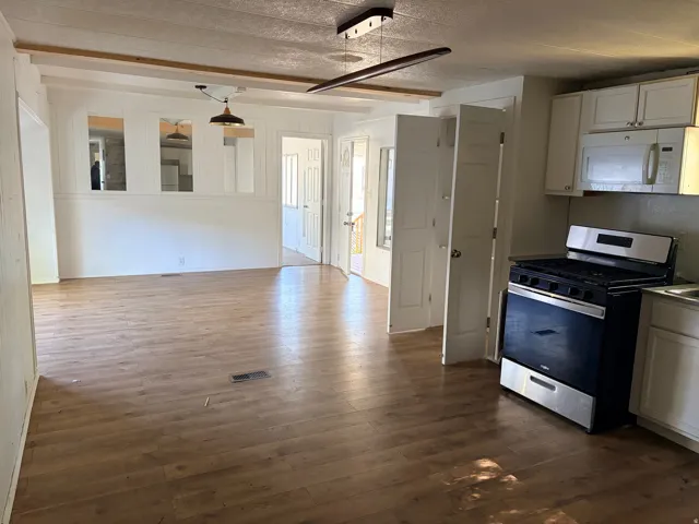 Wood-finish flooring throughout, white paneled walls, white cabinetry, stainless steel oven, and a built-in microwave