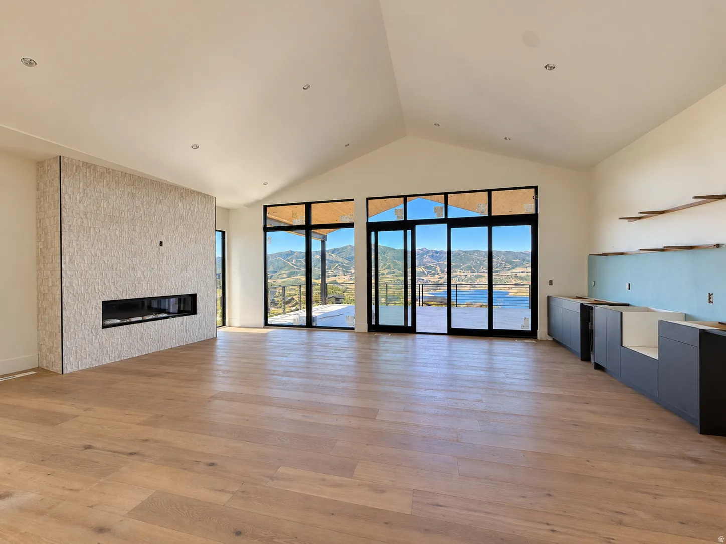 Vaulted ceiling with recessed lighting, linear fireplace with a textured surround, wood-finish flooring, sliding glass doors to outdoor deck, and built-in cabinetry
