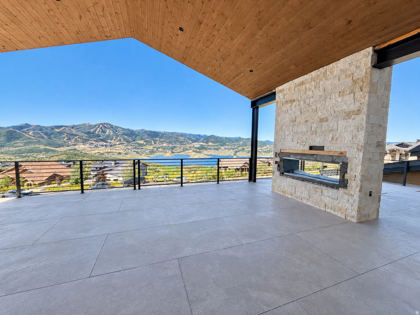 Expansive outdoor terrace with a wood-planked ceiling, stone-clad fireplace, and cable railing system, overlooking a Deer Valley and Jordanelle Reservoir