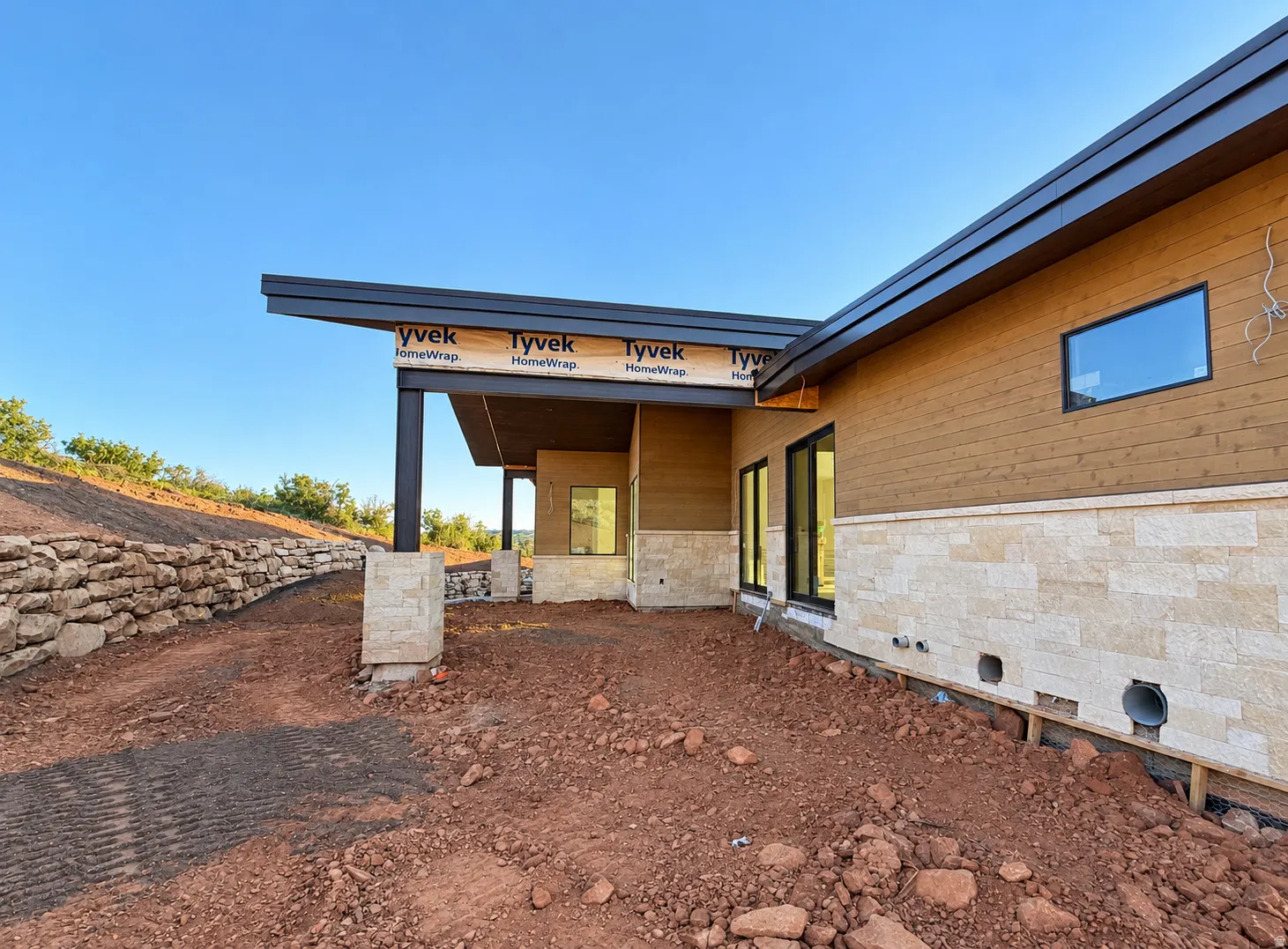 Private Back Patio Modern architectural design featuring a low-slope roofline, a natural stone retaining wall, and horizontal wood-finish siding