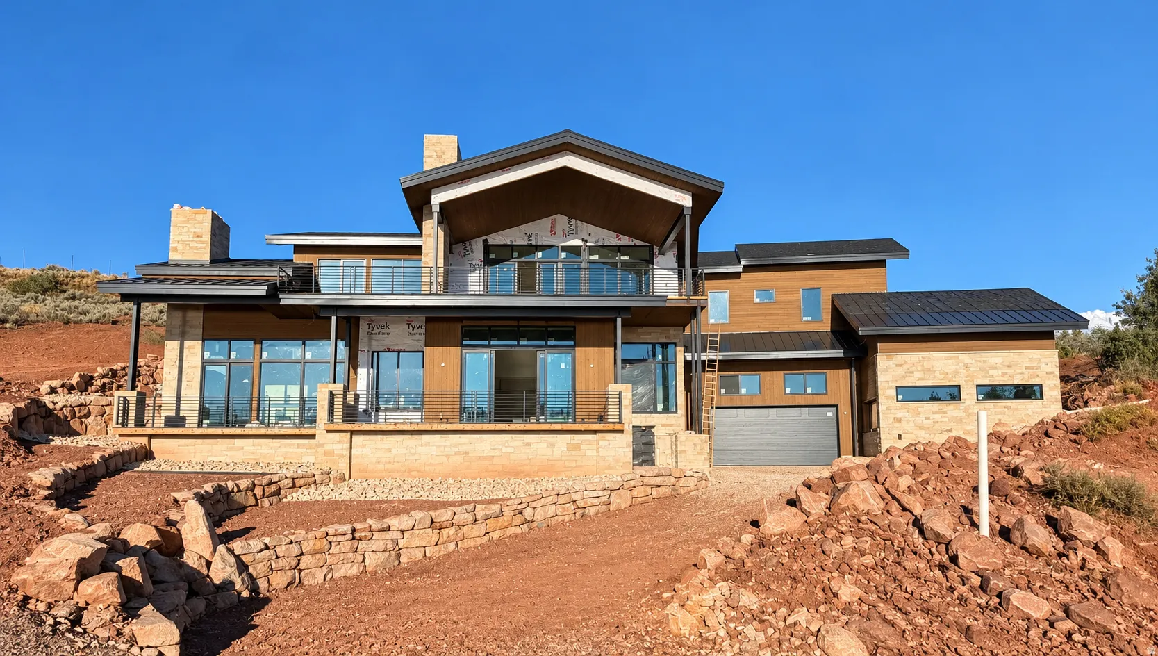 Contemporary architectural style featuring multiple balconies with glass railings, an attached two-car garage, extensive window placement, and stone and wood-panel exterior accents