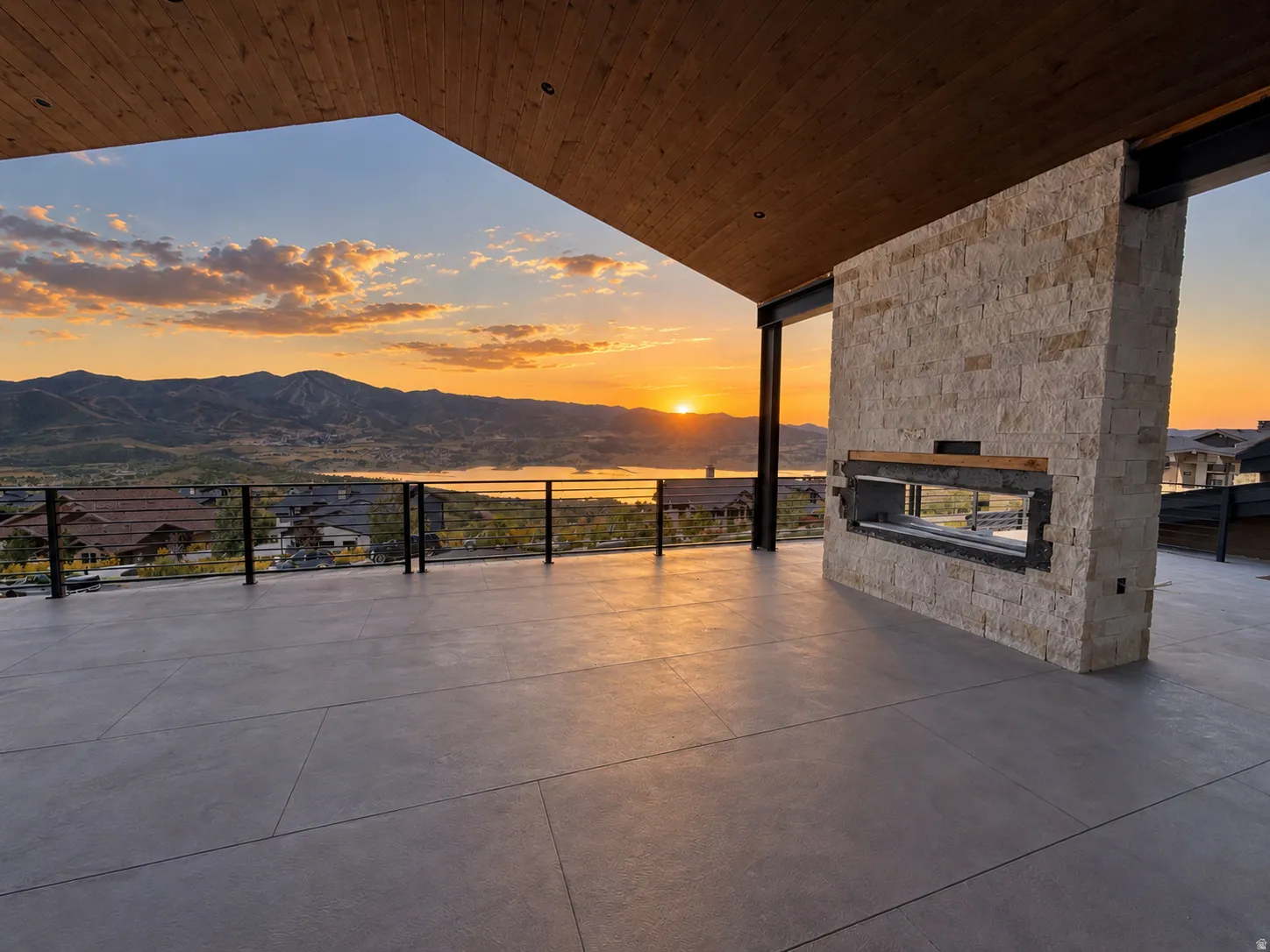 Sunset View. Expansive outdoor patio with concrete flooring, stone-clad fireplace, and wood-paneled ceiling