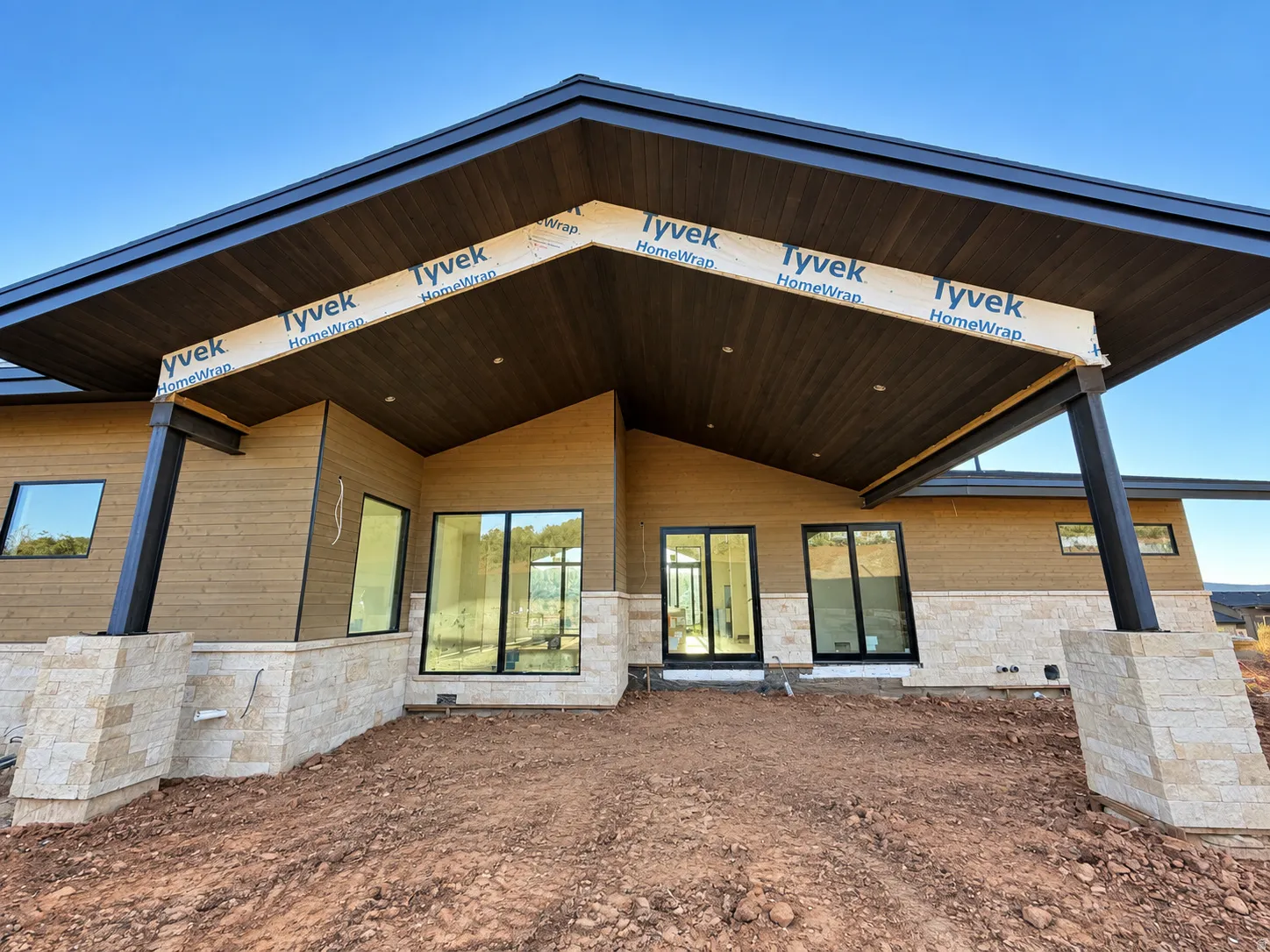 Private back patio  featuring horizontally paneled siding, stone veneer accents, and an expansive dark wood-finish soffit