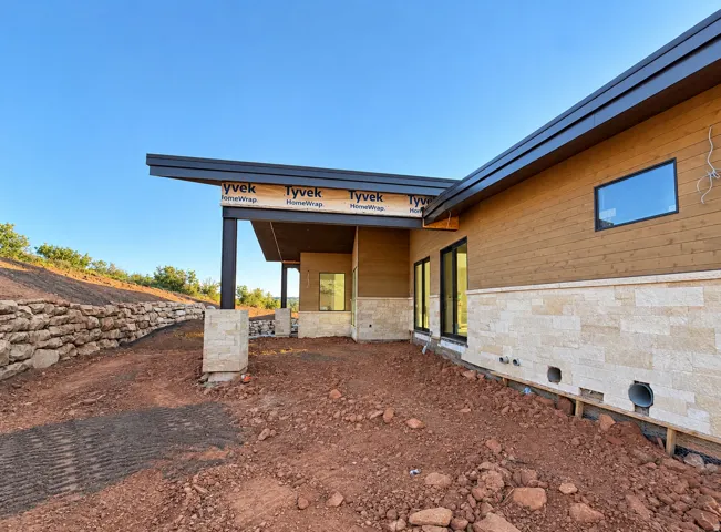 Private Back Patio Modern architectural design featuring a low-slope roofline, a natural stone retaining wall, and horizontal wood-finish siding