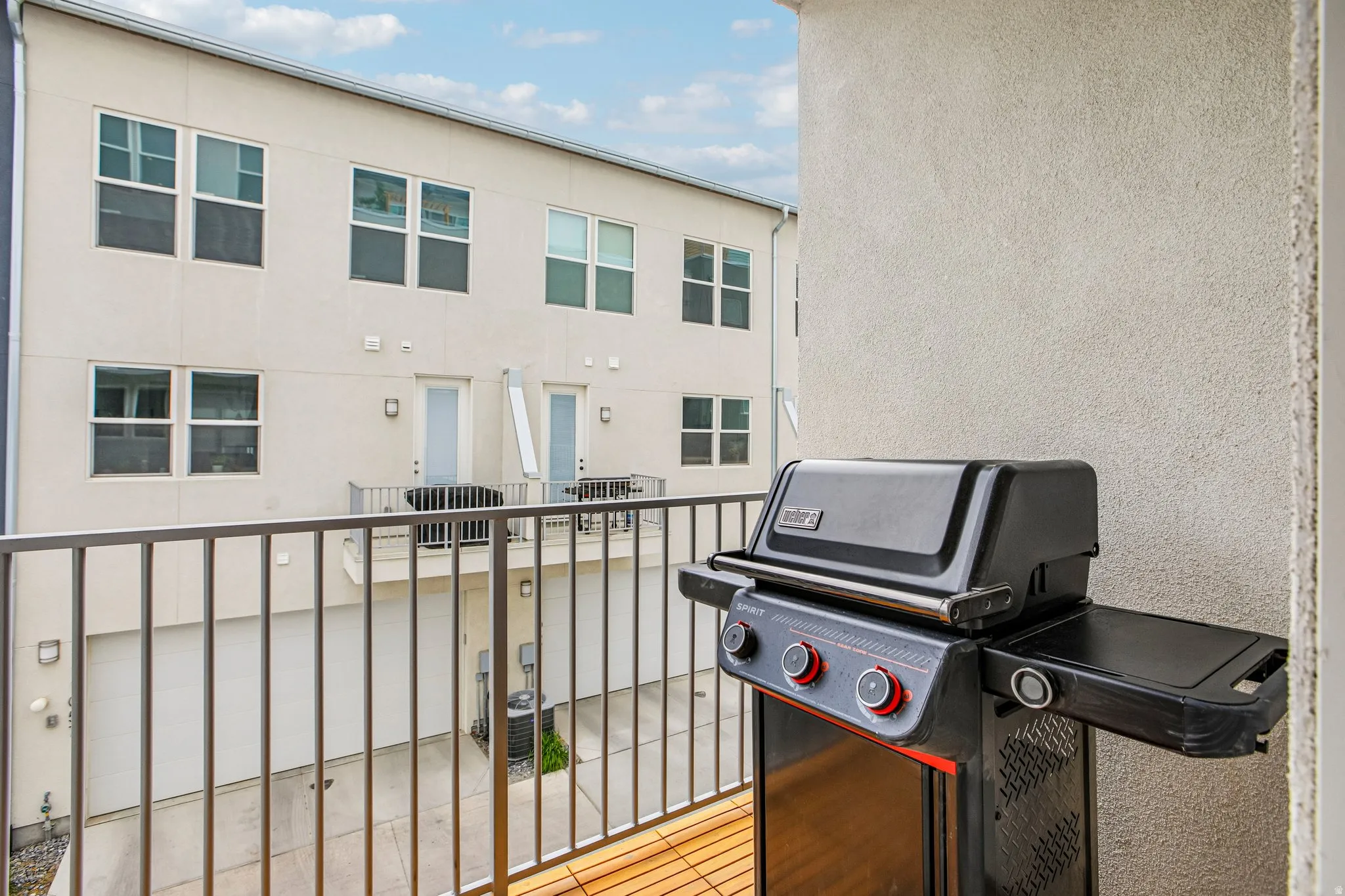 Spacious covered balcony featuring stainless steel gas grill with dual burners and storage shelf, metal railing, and wood-finish decking