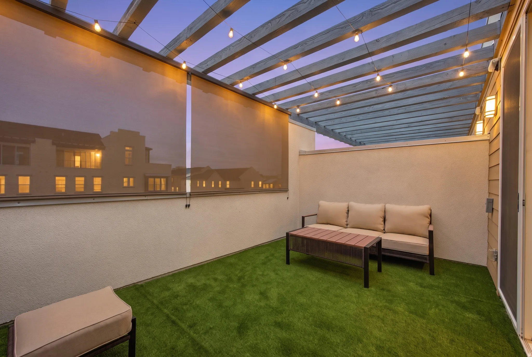 Rooftop patio with artificial turf flooring, wooden pergola, string lighting, and exterior wall sconces
