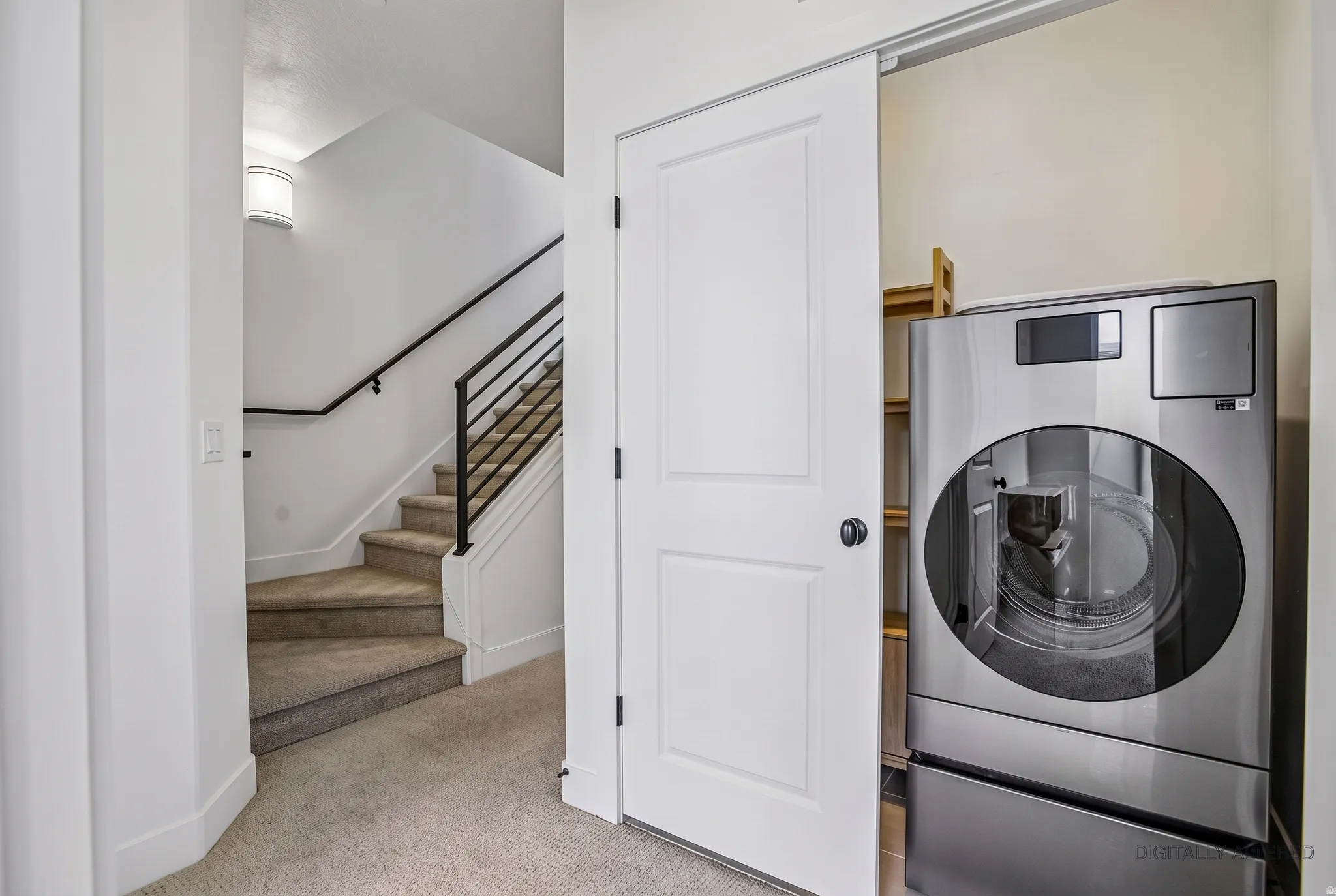Staircase with a black metal railing and carpeted treads, accompanied by a laundry closet featuring a sliding door and built-in shelving