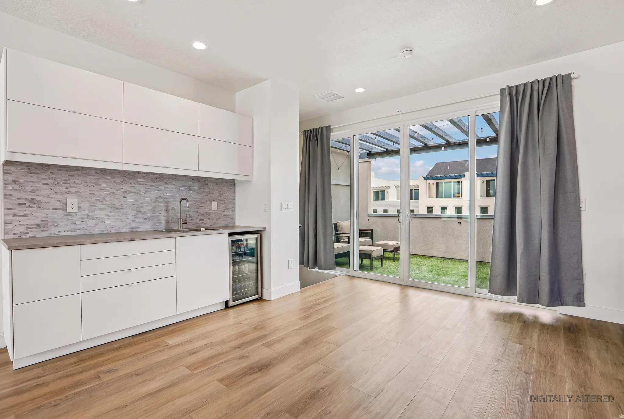 Wood-finish flooring, white cabinetry, tile backsplash, built-in beverage refrigerator, and sliding glass doors leading to an outdoor space