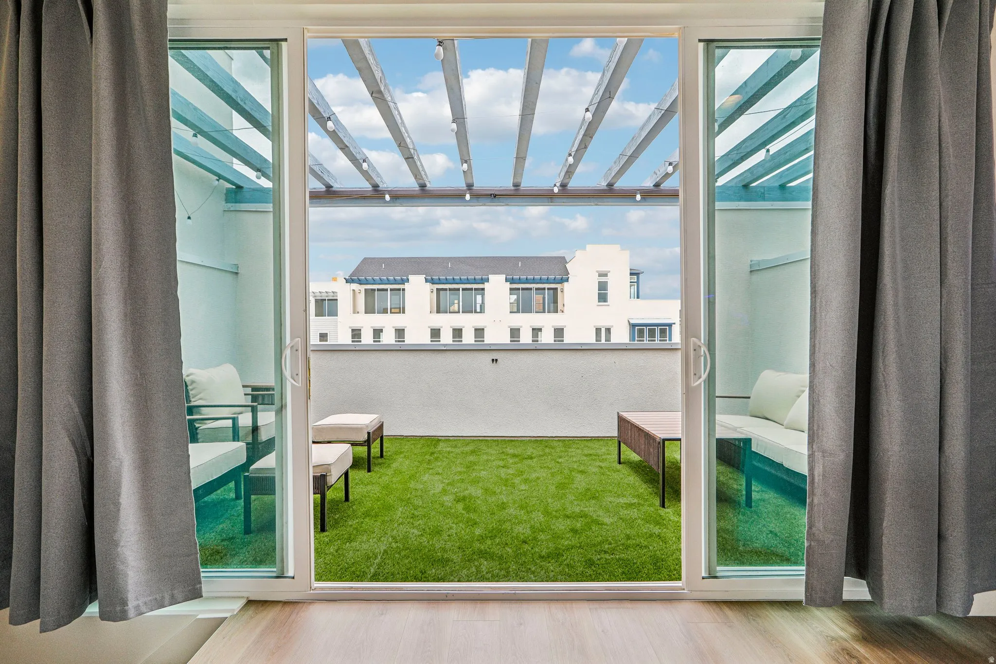 Expansive outdoor patio with artificial turf, overhead pergola, and multiple seating areas