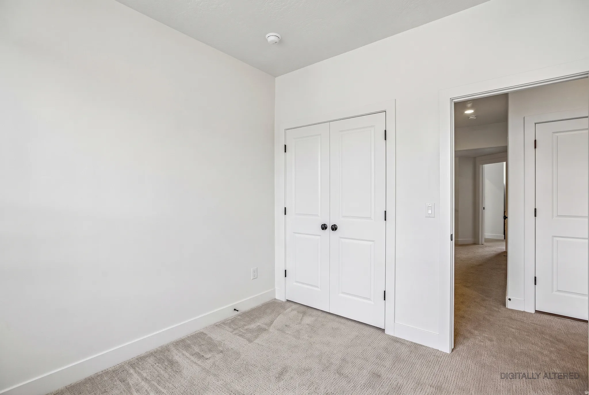 White interior walls with white trim, gray carpet flooring, and a white closet door with black hardware