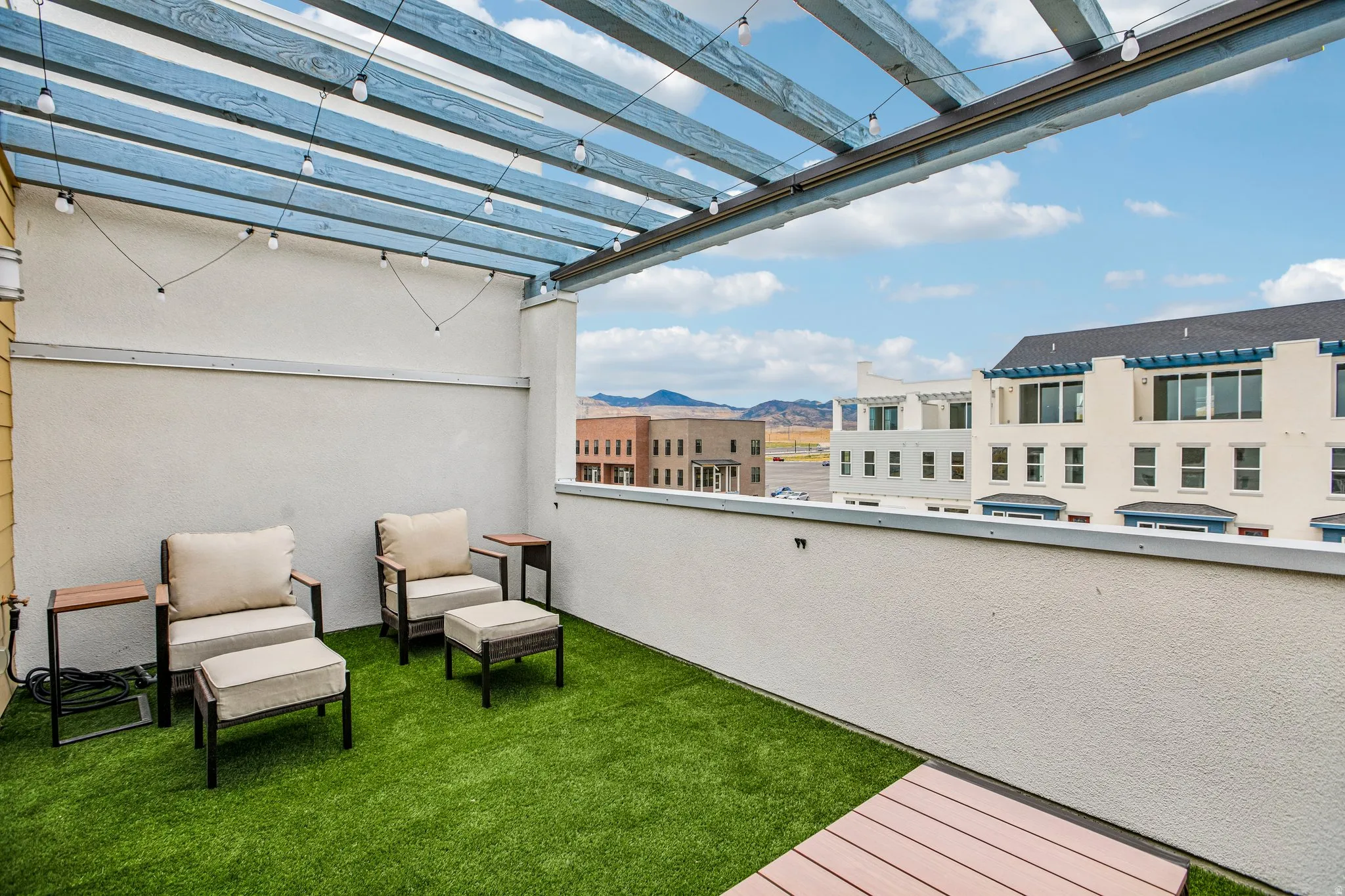 Rooftop patio featuring a blue slatted pergola, string lighting, artificial turf, and a composite decking section