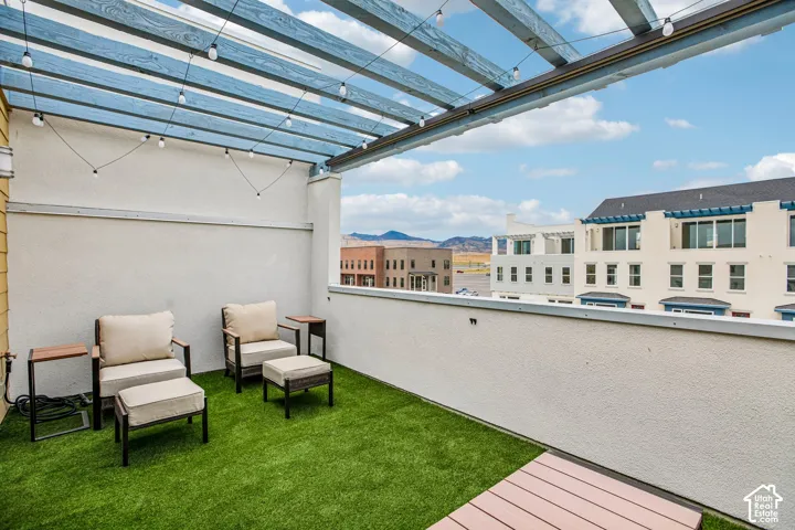 Rooftop patio featuring a blue slatted pergola, string lighting, artificial turf, and a composite decking section