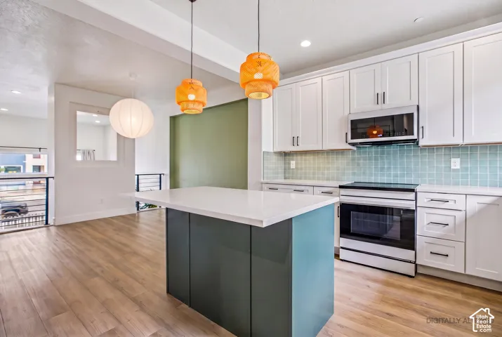 Kitchen featuring a central island with white countertop, light wood-finish flooring, white cabinetry, integrated stainless steel appliances, and a tiled backsplash