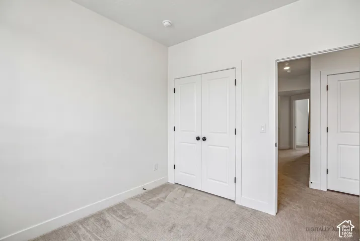 White interior walls with white trim, gray carpet flooring, and a white closet door with black hardware