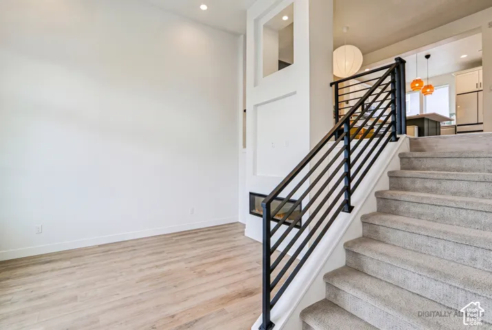 Modern interior with wood-finish flooring, a linear fireplace, and a carpeted staircase with an iron railing