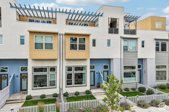 Contemporary exterior featuring multi-toned siding, expansive windows, pergolas, and a white picket fence