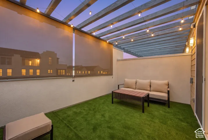 Rooftop patio with artificial turf flooring, wooden pergola, string lighting, and exterior wall sconces