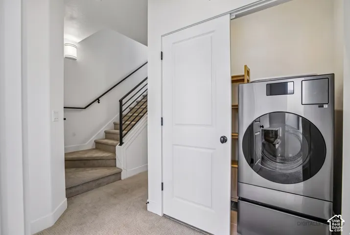 Staircase with a black metal railing and carpeted treads, accompanied by a laundry closet featuring a sliding door and built-in shelving