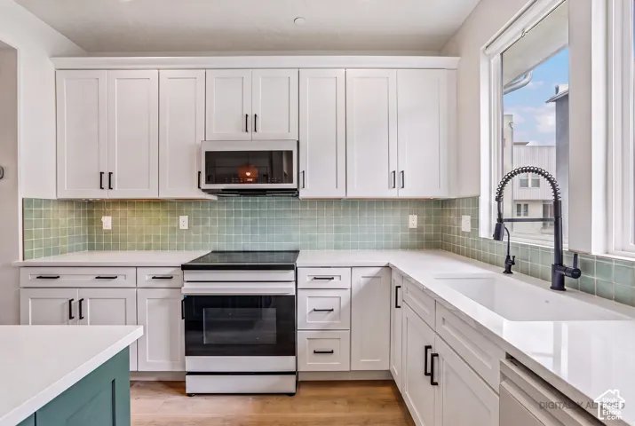 White shaker cabinetry with matte black hardware, light green tile backsplash, white countertops, and wood-finish flooring