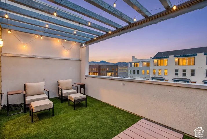 Outdoor terrace featuring a slatted pergola with string lighting, artificial turf surfacing, and a defined railing