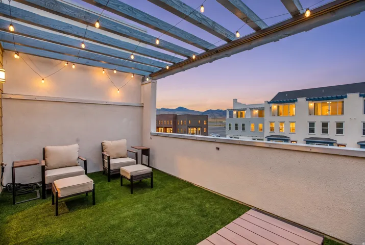 Outdoor terrace featuring a slatted pergola with string lighting, artificial turf surfacing, and a defined railing