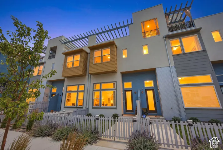 Contemporary townhomes featuring a multi-story facade, prominent windows, and a white picket fence